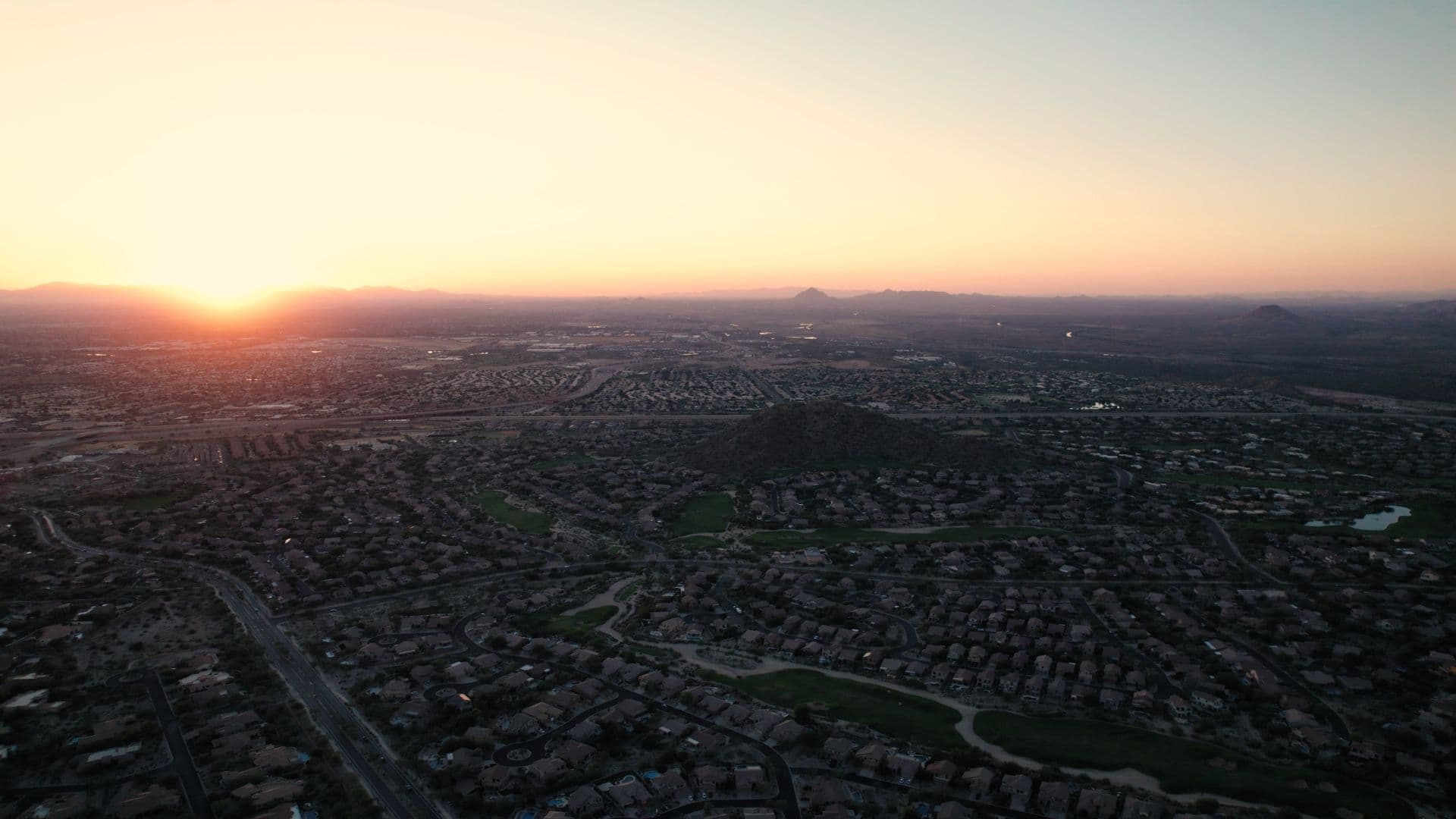 Aerial panoramic view of a suburban neighborhood at sunset with orange sky on the horizon